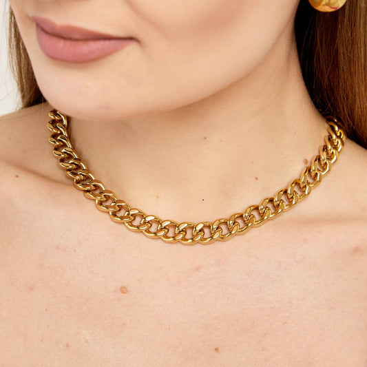 A close-up image of a woman wearing a gold-colored Cuban choker necklace.