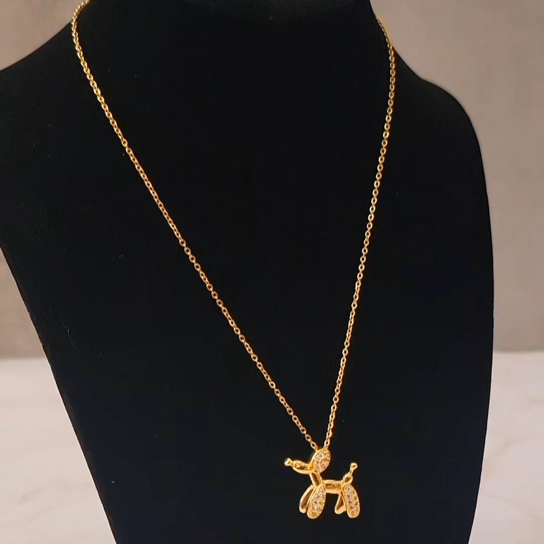 Minimal gold jewelery with, a balloon dog pendant on a display.