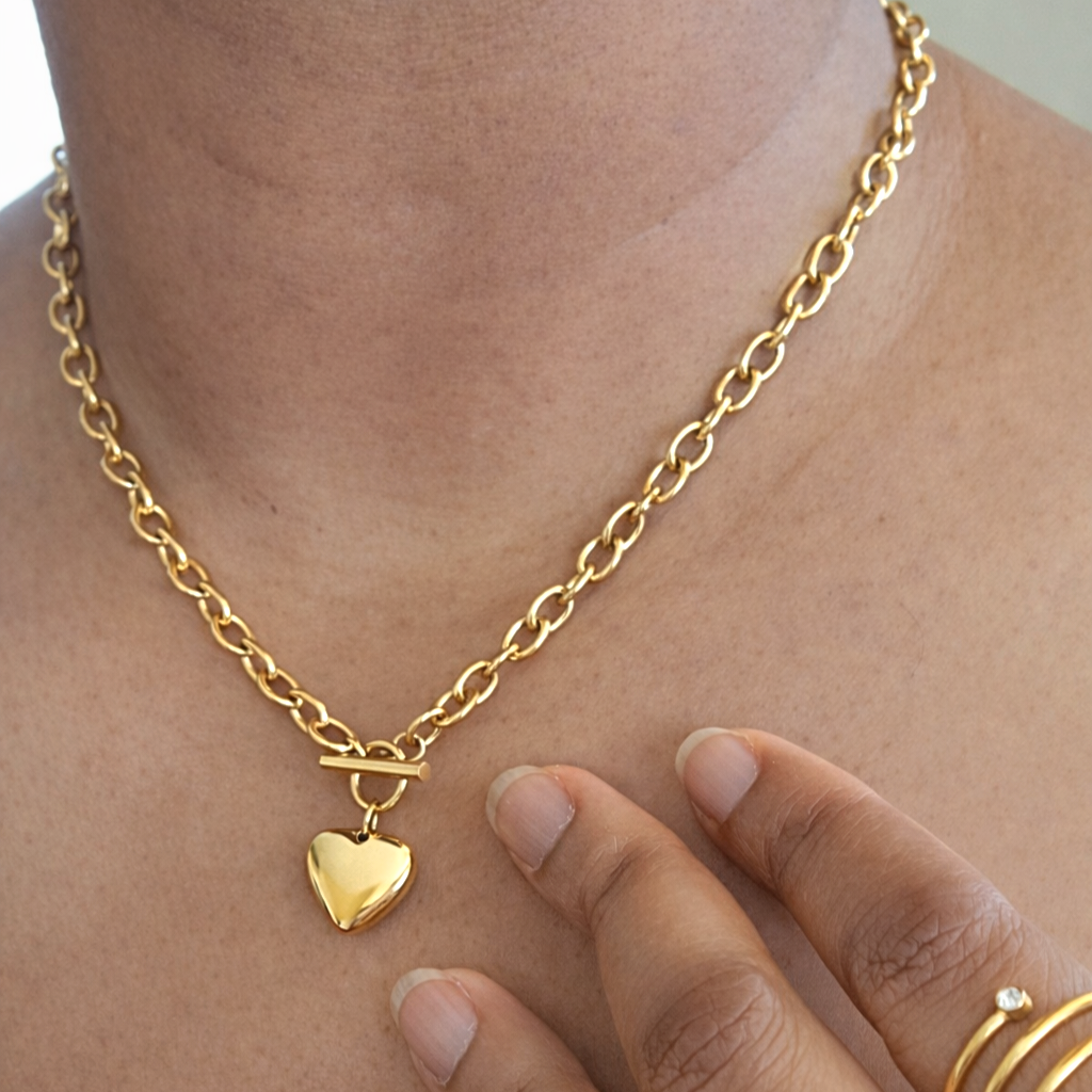 Gold link chain necklace with a heart-shaped pendant on a models neck.