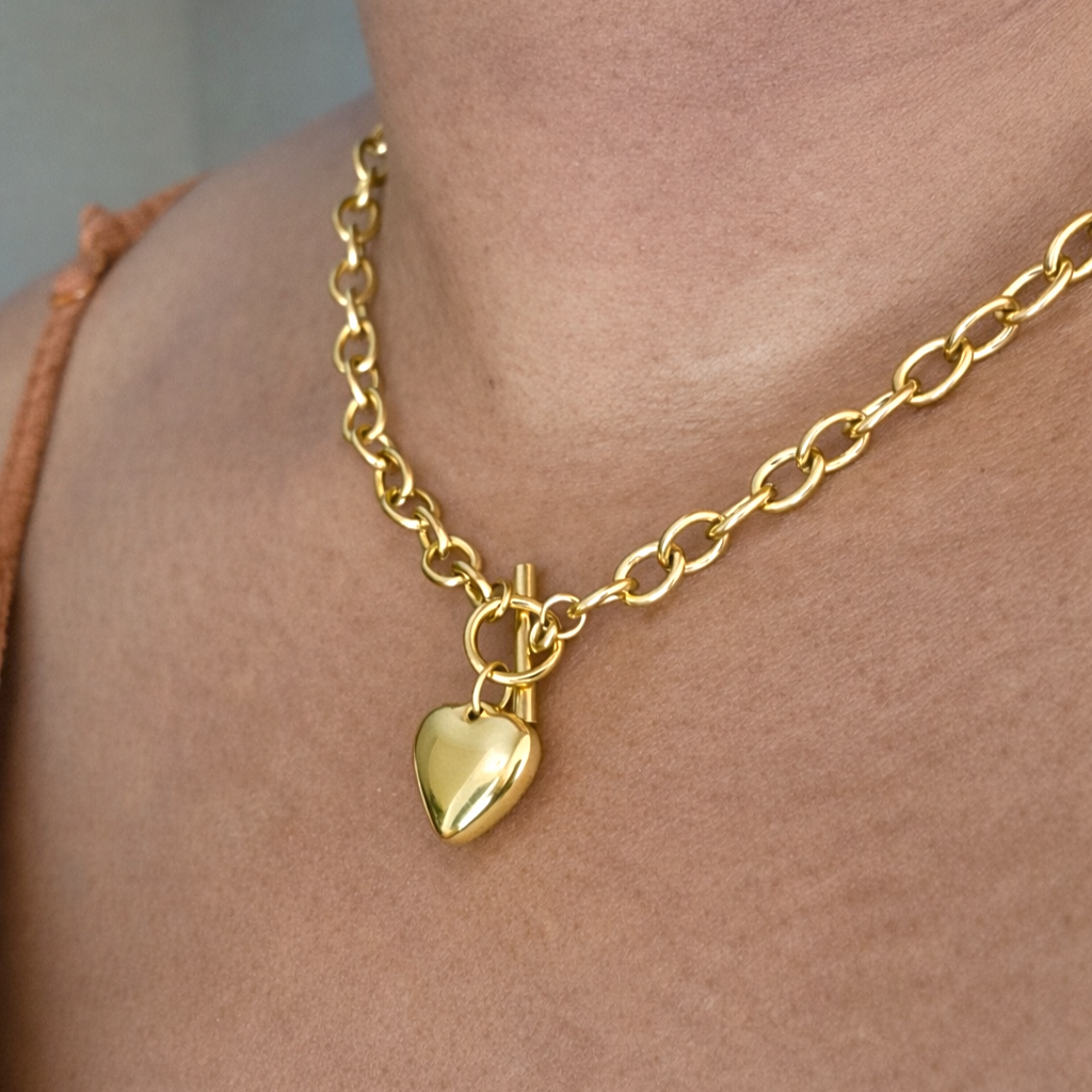 Gold link chain necklace with a heart pendant on a models neck.