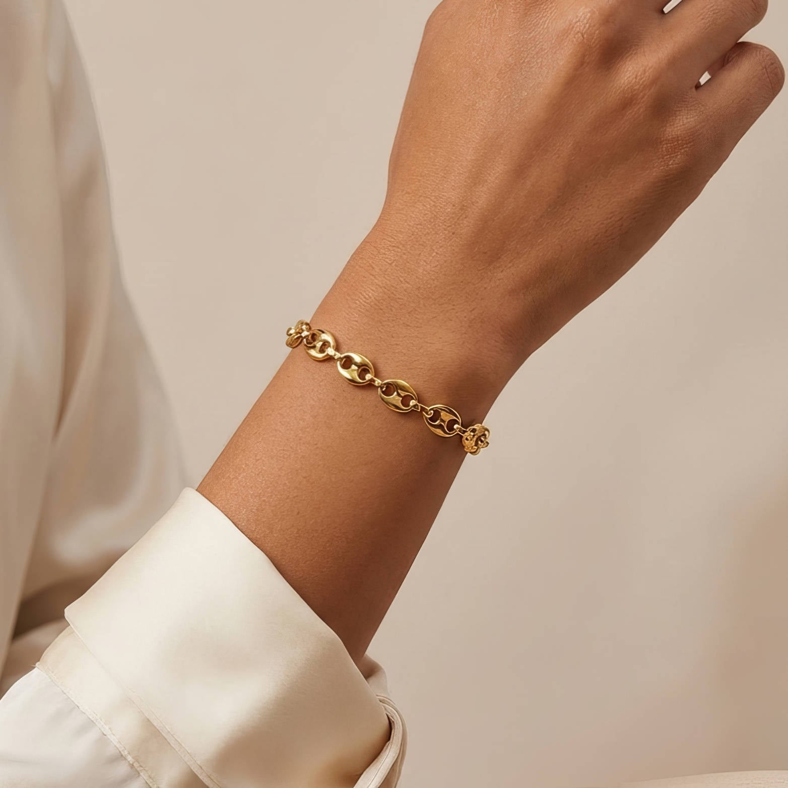 Gold chain bracelet on a wrist with a neutral background